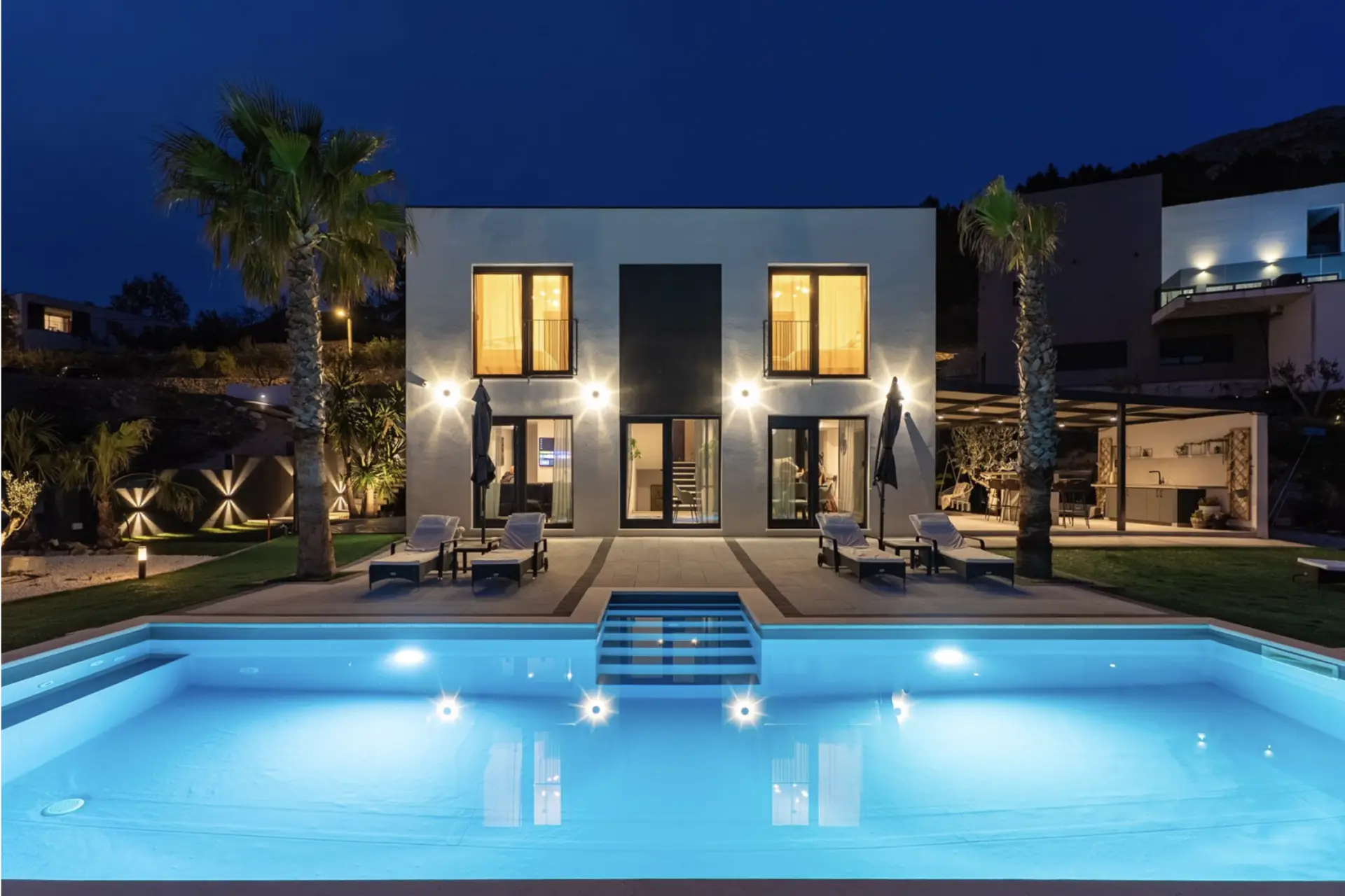 villa with two palm tress next to the pool by night