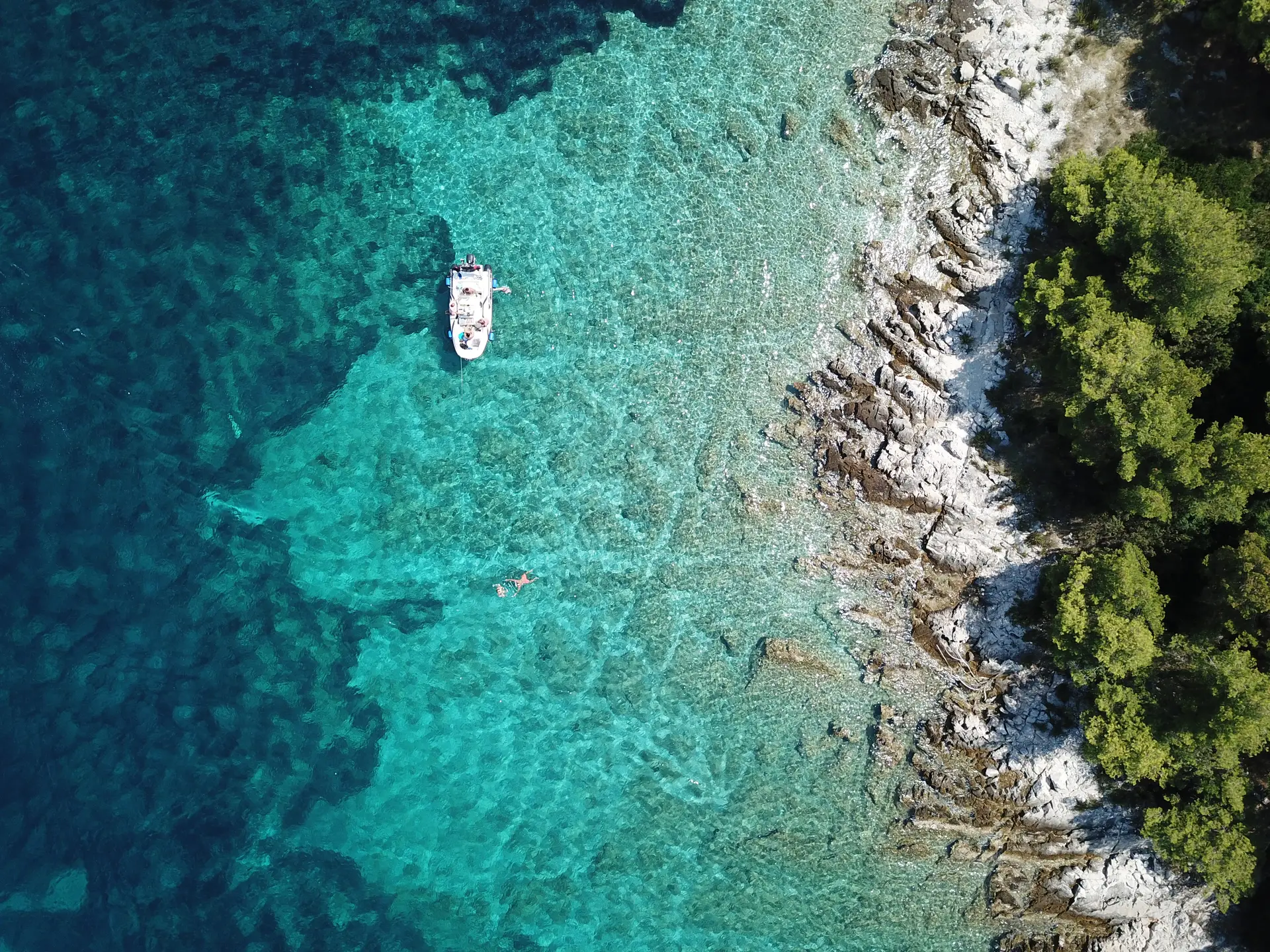 aerial view of a boat floating in the sea next to the rocky shore