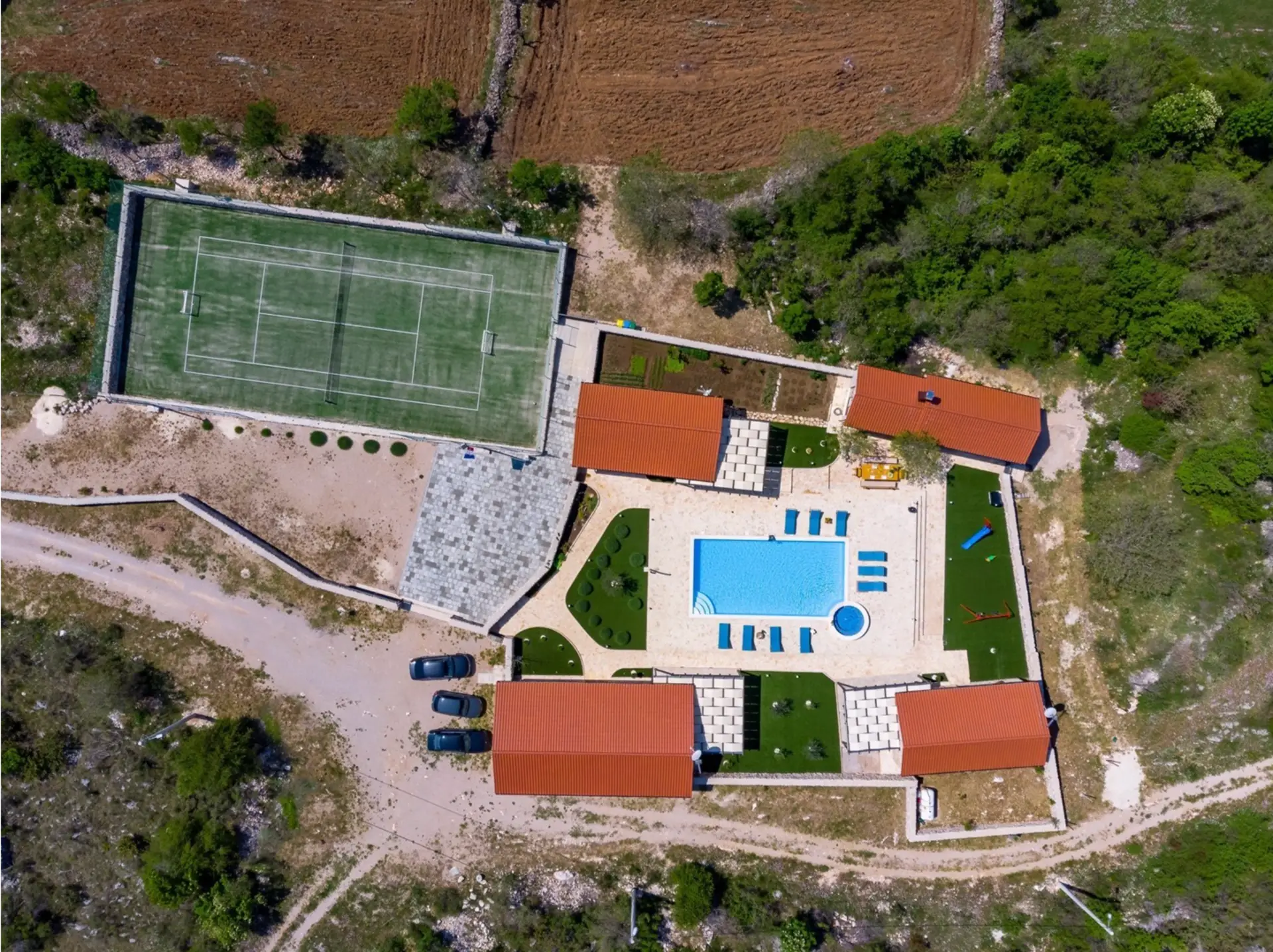 Luftaufnahme eines Anwesens mit 4 Häusern, Pool und Tennisplatz