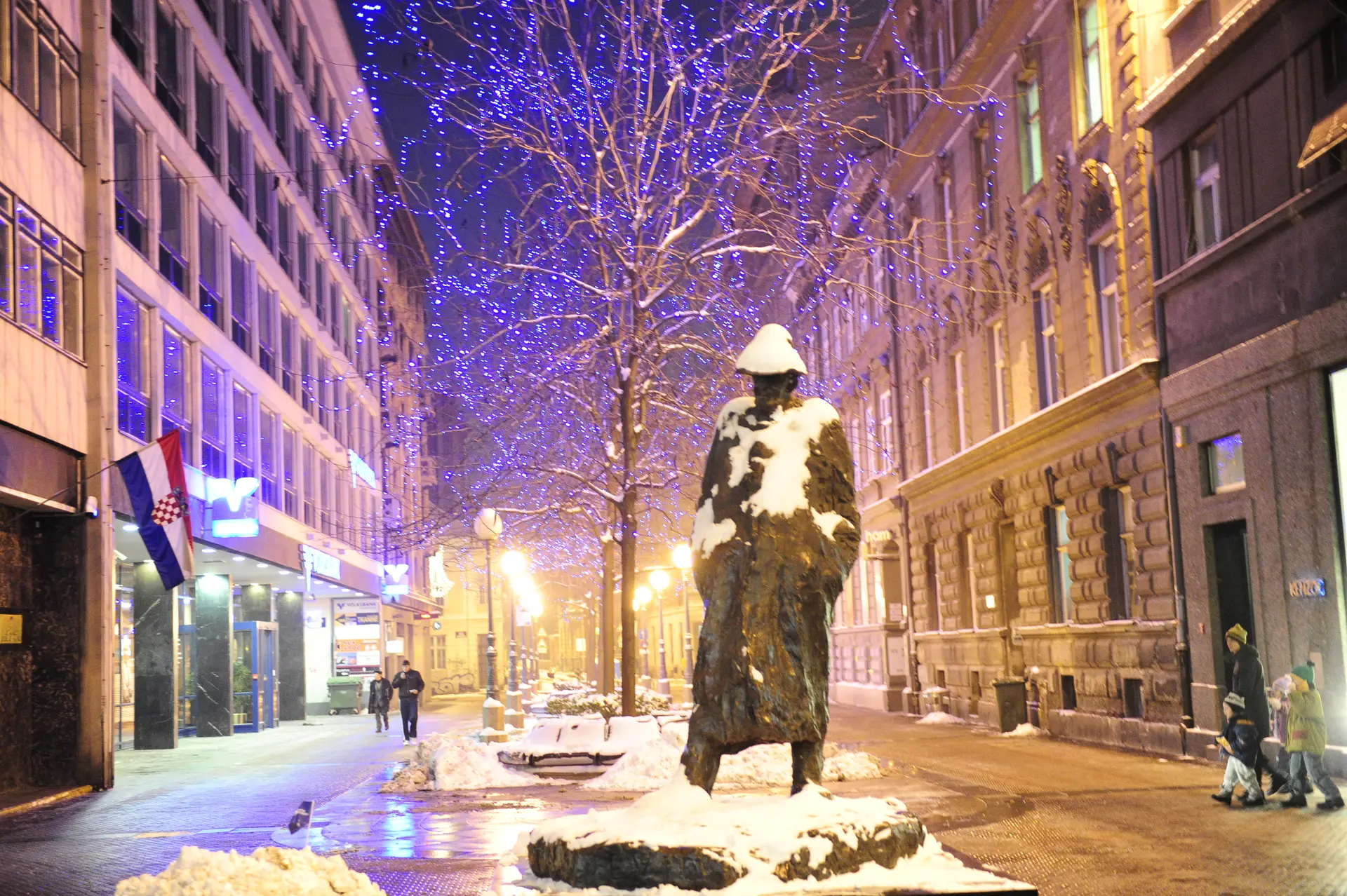 statue with a snow on it in the town decorated by lights