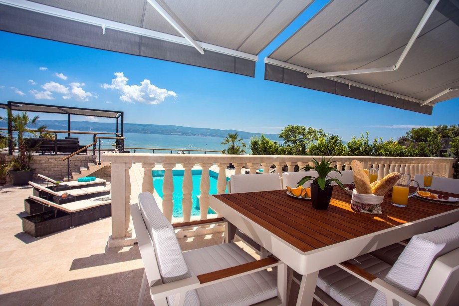 Outdoor dining area with sea and pool view, connected with a kitchen