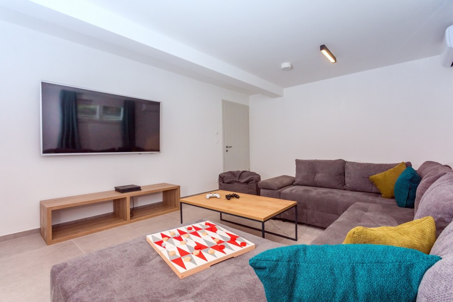 Media room with a larger TV, PS4, sofas, and A/C on the lower ground floor.