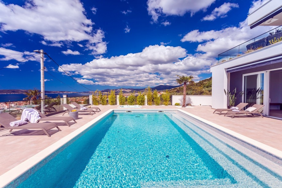 The pool and sun deck area is surrounded by palm and olive trees.