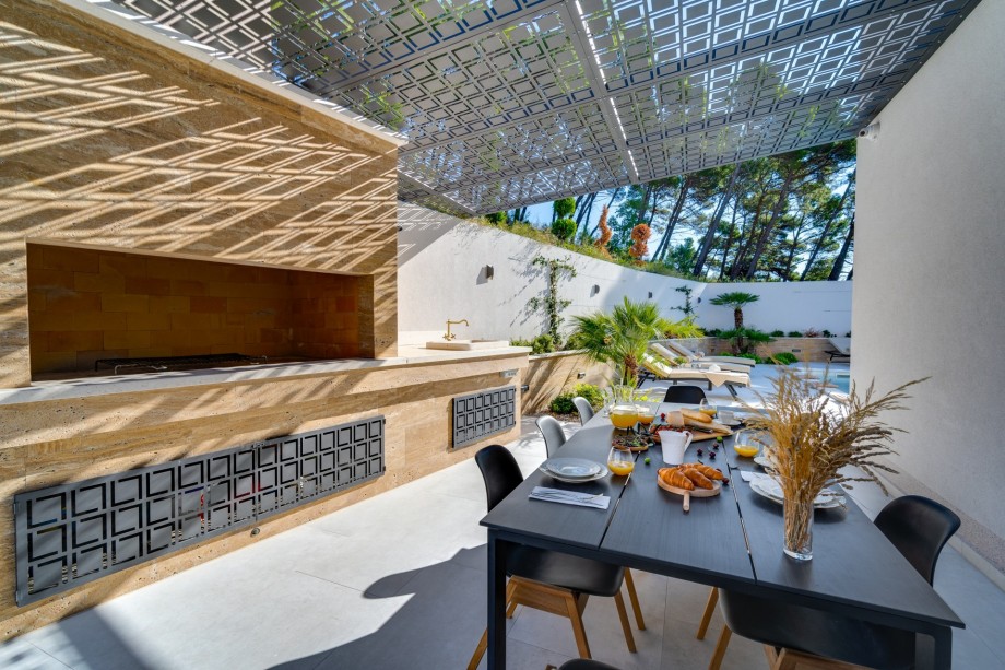 A covered outdoor dining area for 8 people with a traditional barbecue.