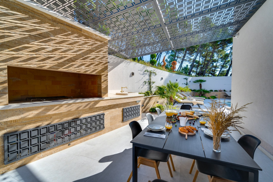 A covered outdoor dining area for 8 people with a traditional barbecue.