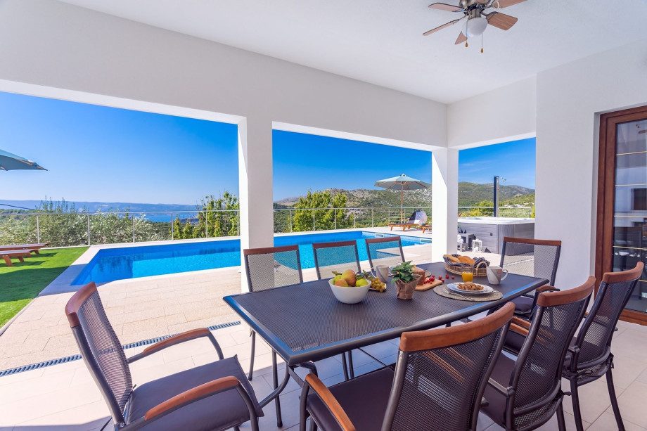 Covered outdoor dining area for 8 with a TV and traditional BBQ next to it.