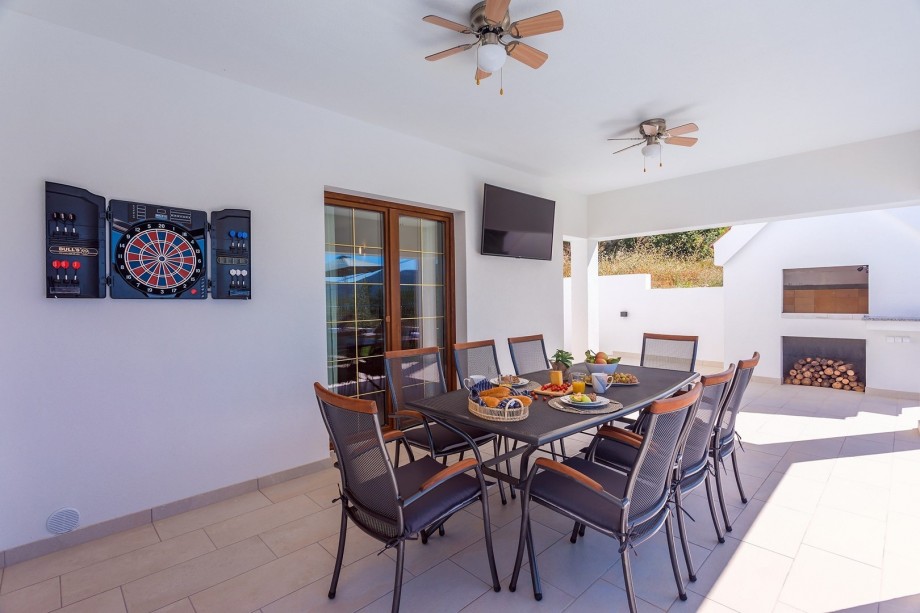 Covered outdoor dining area for 8 with a TV, darts for fun and a traditional BBQ next to it