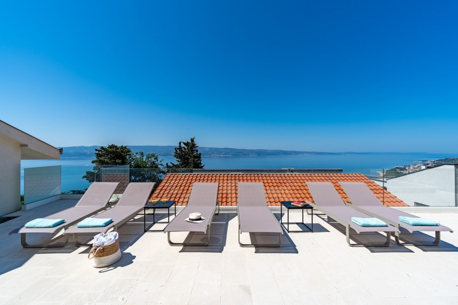 A sun deck area with 6 deck chairs, additional 6 patio chairs and the dining table with sun-umbrellas