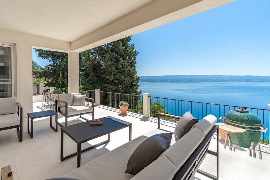 The outdoor at the 1st floor level is located in front of the living area and offers a large wooden dining table for 12 people and a Kamado Joe grill