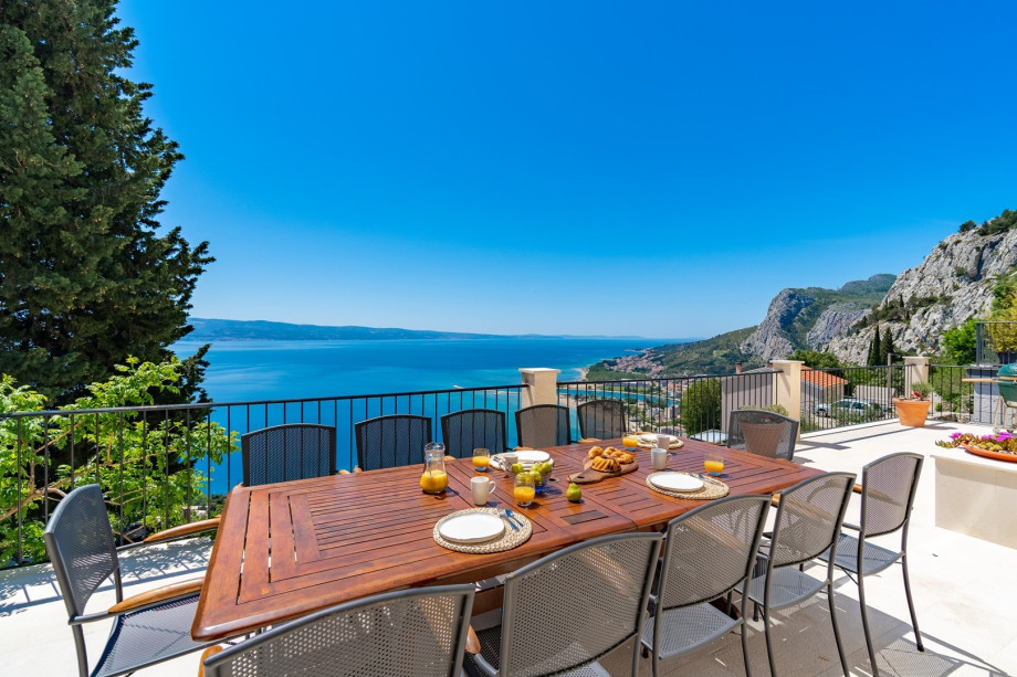 The outdoor at the 1st floor level is located in front of the living area and offers a large wooden dining table for 12 people and a Kamado Joe grill, with panoramic sea views giving you a re