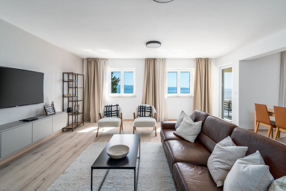 Spacious living area (40sqm) with comfortable sofa, TV, A/C, a panoramic window, a fully equipped kitchen