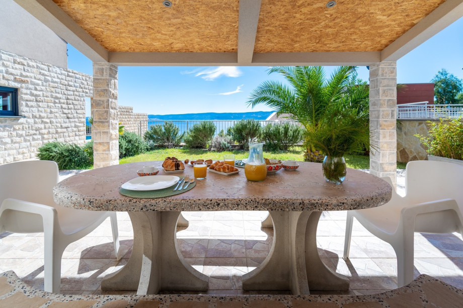 Outdoor dining area with furniture next to the grill, open sea view