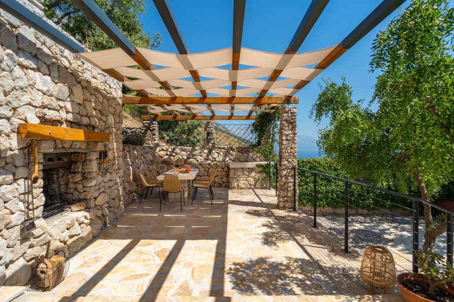 Covered and not overlooked outdoor dining area with a stone table and a traditional barbecue (woods, charcoal) next to it, all in front of the kitchen