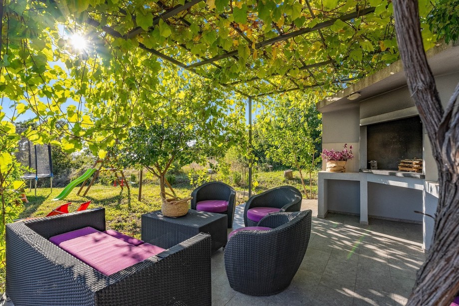 Comfortable lounge corner next to a traditional barbecue all with natural shade
