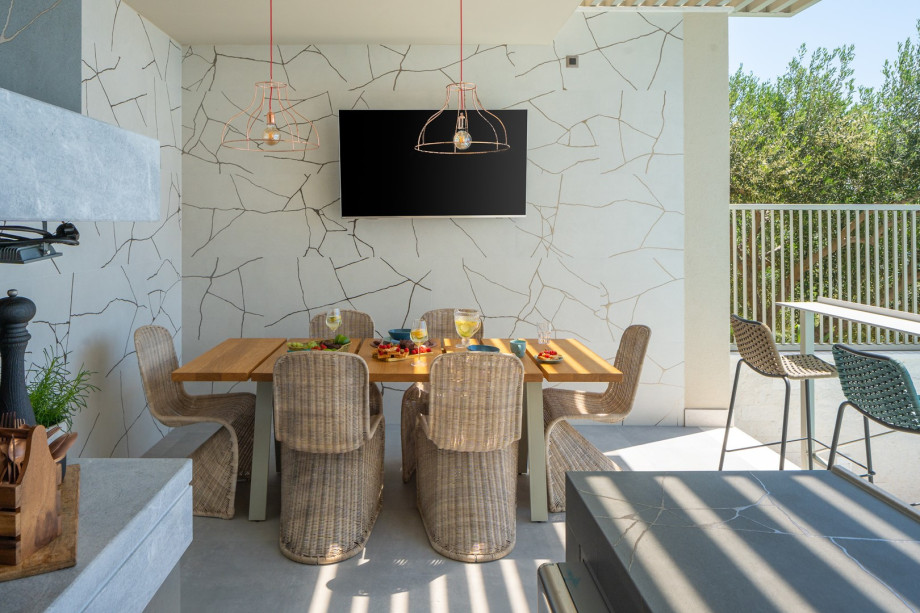 A summer kitchen  with a barbecue, covered dining space with a TV and 4 bar chairs