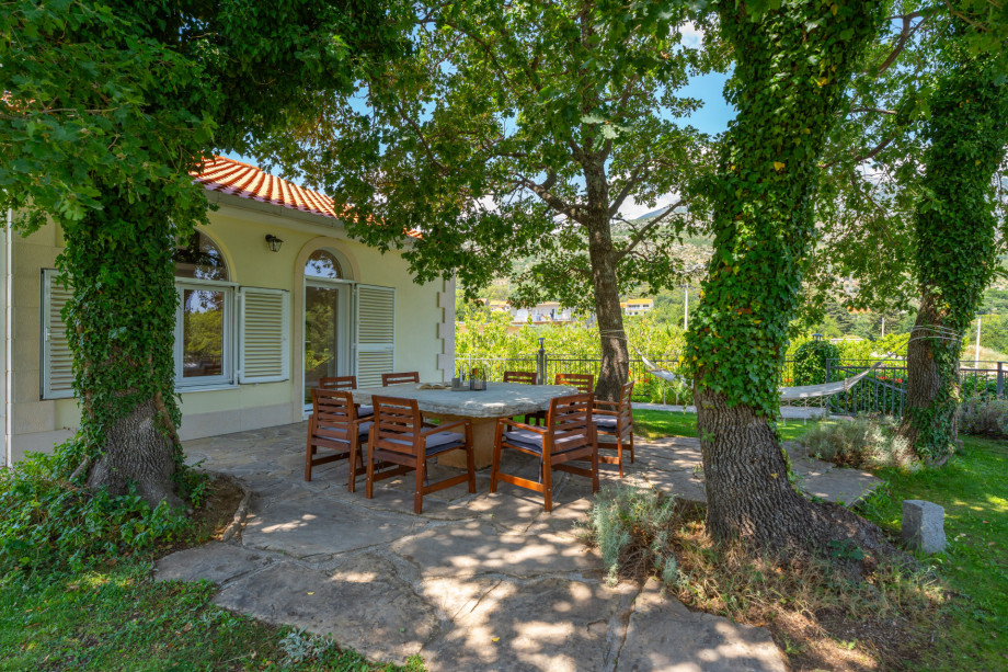 A shaded outdoor dining area with a stone table and oak trees