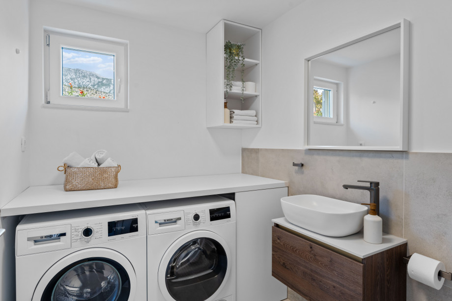 laundry with washing machine, dryer, ironing amenities and a toilet - next to the kitchen area