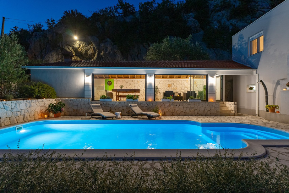 Private pool with covered dining and sitting area at night