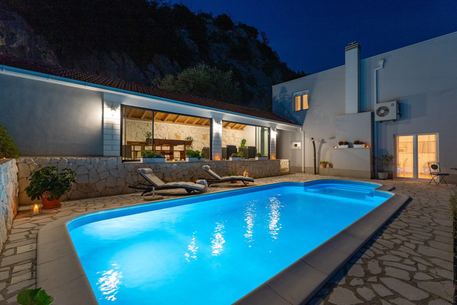 Private pool with covered dining and sitting area at night