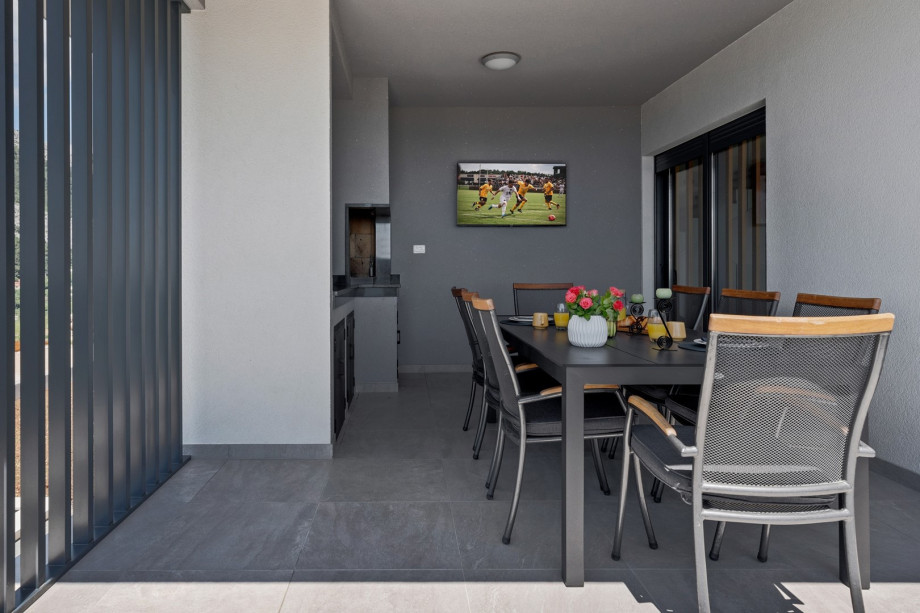 a covered outdoor dining area with a traditional barbecue (woods, charcoal) and a flat screen TV