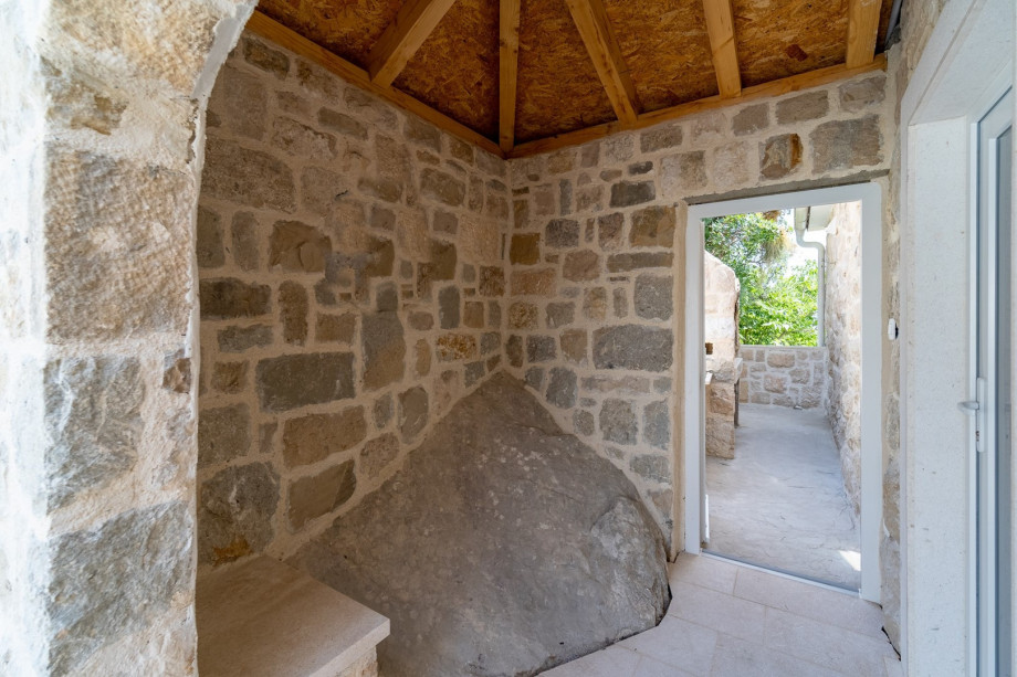 A traditional barbecue is located next to the main entrance to the house, next to the outdoor dining area.