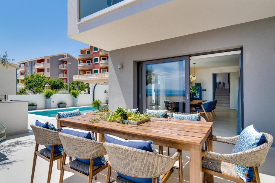 An outdoor dining area with a dining table for 8 people with a barbecue, a TV and a fridge