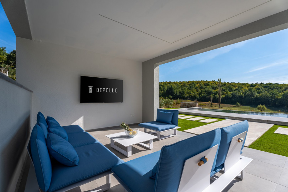 Überdachter Bereich mit einer Loungeecke, einem Flachbildfernseher, ein paar Liegestühlen mit Sitzsäcken und einer Bar