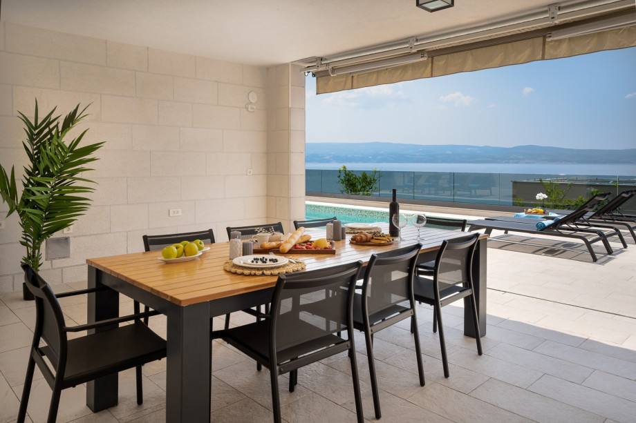 Covered outdoor dining area with BBQ and speakers, between pool and living area