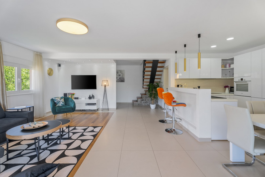 The living room with a flat-screen TV, glass walls toward the terrace with outdoor dining area
