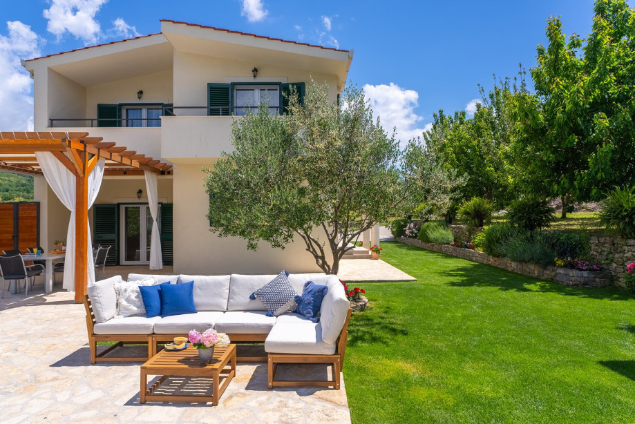 The outdoor area features table soccer, a large grass plot with a trampoline, a badminton net, a wooden playhouse with a slide, and a fun zone for young children.