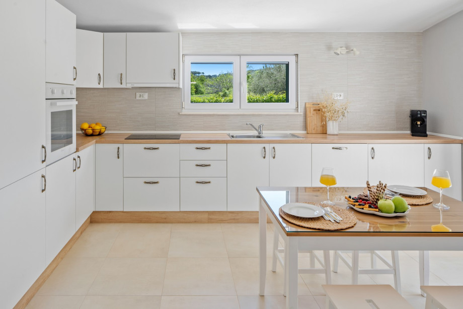 A modern kitchen with white cabinets, wooden countertops, and a window overlooking greenery