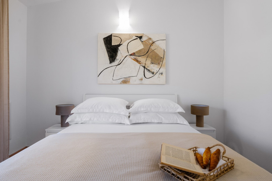 A bright, modern bedroom with a large wardrobe, and glass doors opening to a balcony with views of green hills