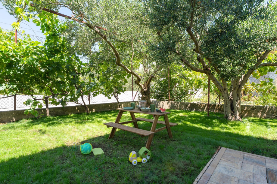 Eine Rasenfläche mit Kinderbereich mit Spielzeug, Schaukel und Sitzecke für Kinder.