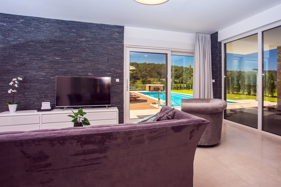 A living room with TV, and exit to a pool and outdoor dining area.
