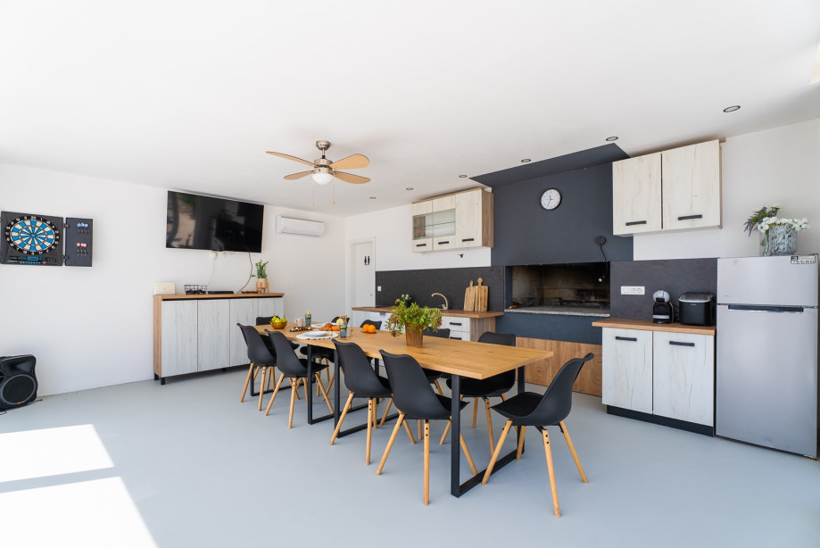 A summer kitchen with a dining table, dishwasher, TV, and darts
