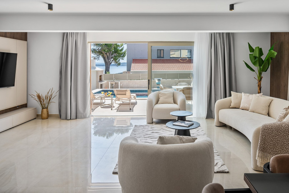 A very bright living room with sofa, flat screen TV, and sliding doors toward the pool area