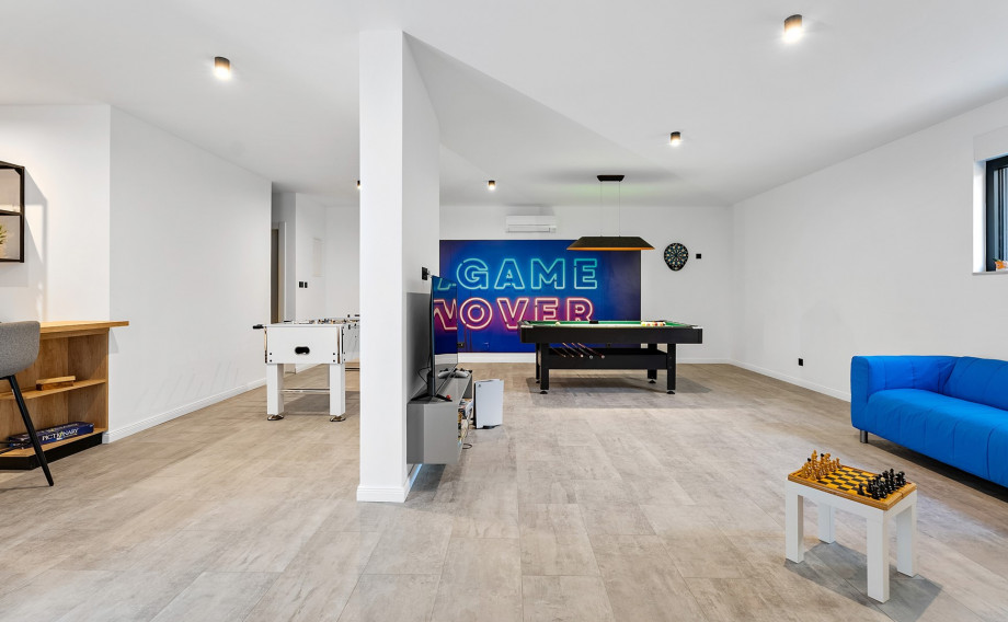 A modern game room featuring a pool table, a foosball table, a large TV with board games underneath.