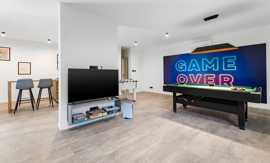 A stylish entertainment space equipped with various board games, a flat-screen TV, bar stools, and classic games like pool and foosball, perfect for relaxing and having fun