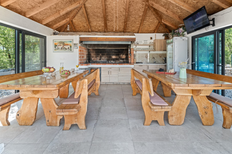 A fully equipped summer kitchen with traditional barbecue area, dining tables, a TV and a separate toilet.