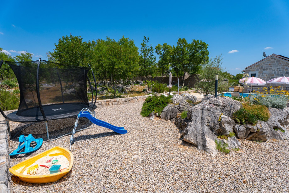 There is a playground in front of the house with a slide and trampoline