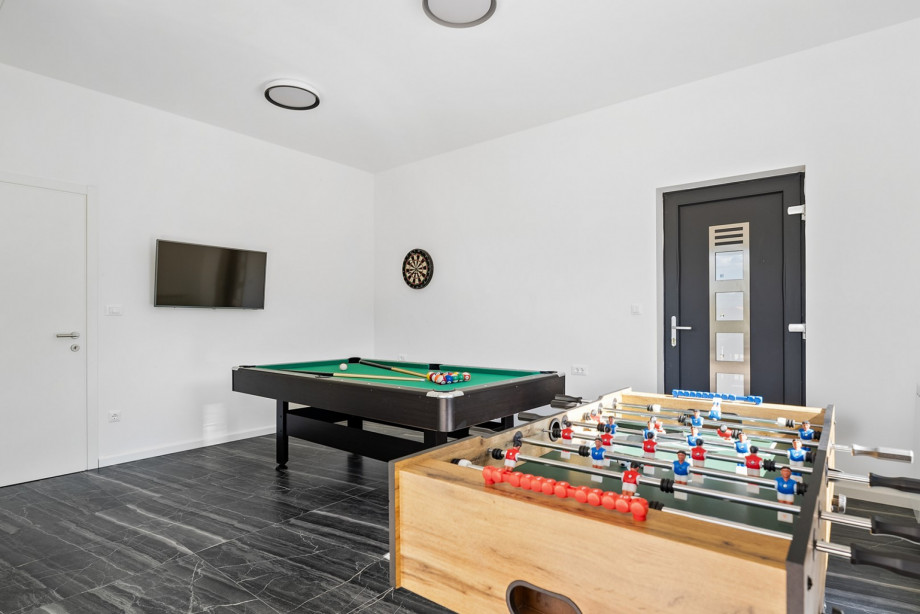 A billiards (pool table), darts, TV, table soccer, and sliding door leading to the pool