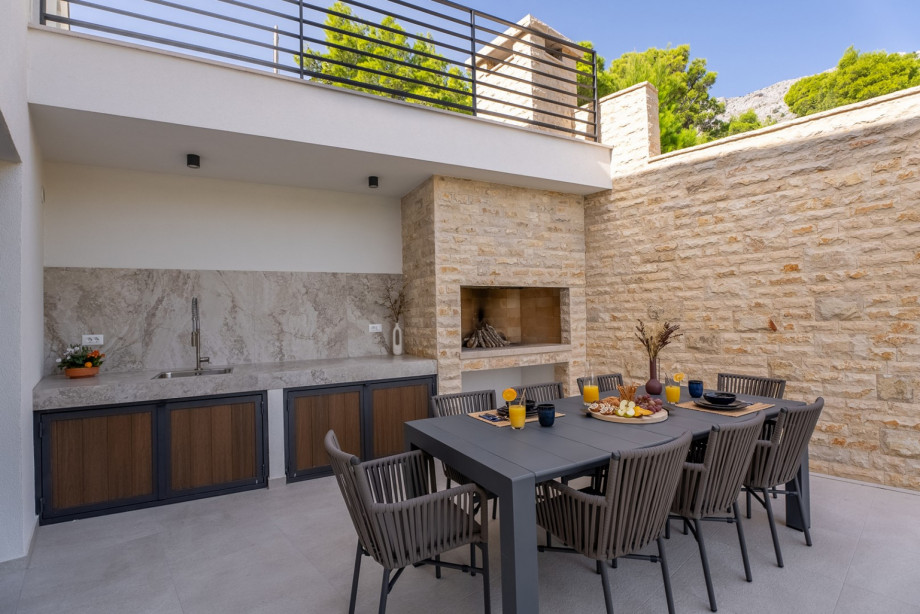 Outdoor dining area with a barbecue overlooking the mountains and the sea.