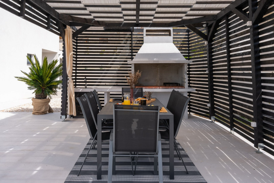Covered outdoor dining area with a traditional barbecue, and a table for 8 people.