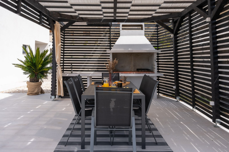 Covered outdoor dining area with a traditional barbecue, and a table for 8 people.