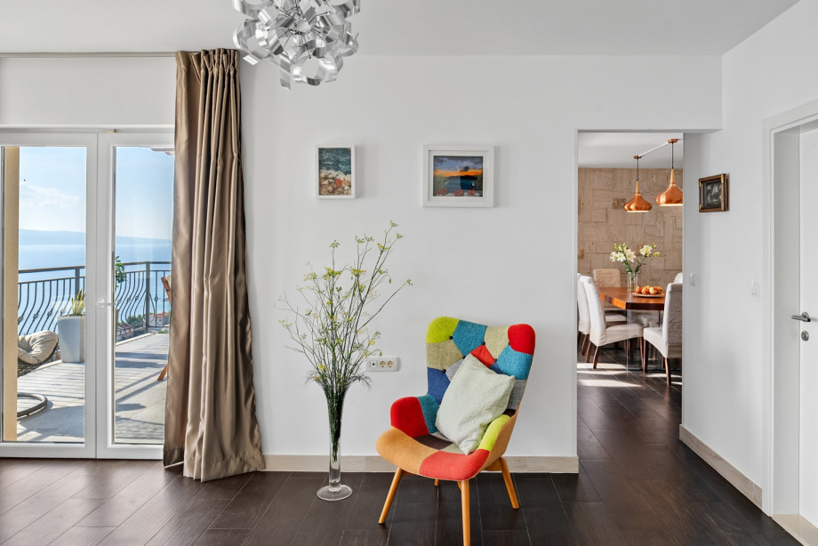 A colorful patchwork armchair provides a vibrant focal point in the hallway, leading towards the dining area and the balcony with sea views