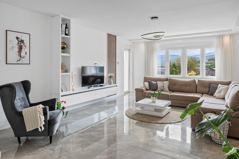 Das geräumige Wohnzimmer lädt zum Entspannen ein und bietet ein gemütliches Sofa, einen Fernseher und einen Ausblick auf die Umgebung.