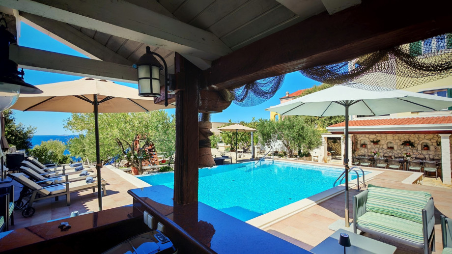 The covered bar area, complete with nautical netting and ample shade, offers a perfect spot for beverages while overlooking the private pool.