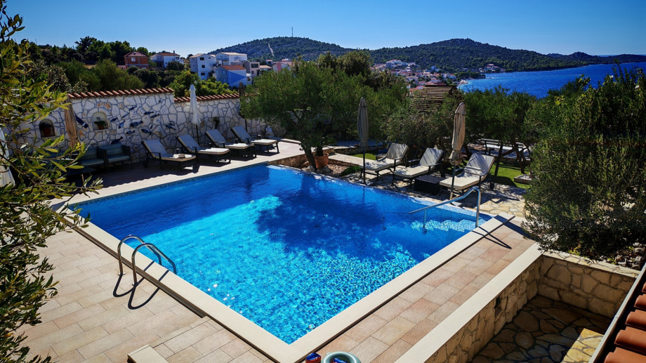 An elevated view captures the large private swimming pool and sun deck, showing the expansive stone terrace and the surrounding charming neighbourhood and sea.