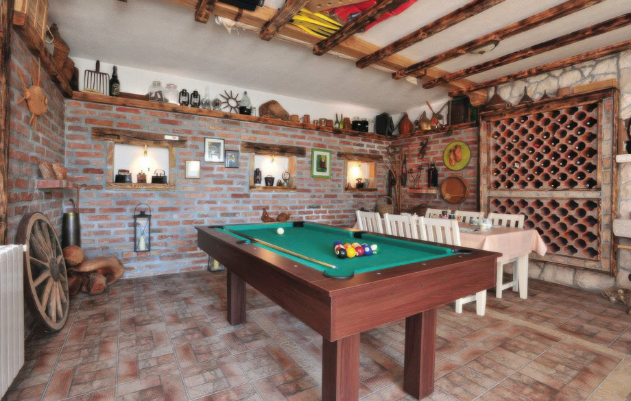 The billiard room (34 sqm) provides indoor entertainment with a pool table, an extra dining table, and a rustic decor featuring a large wine rack.