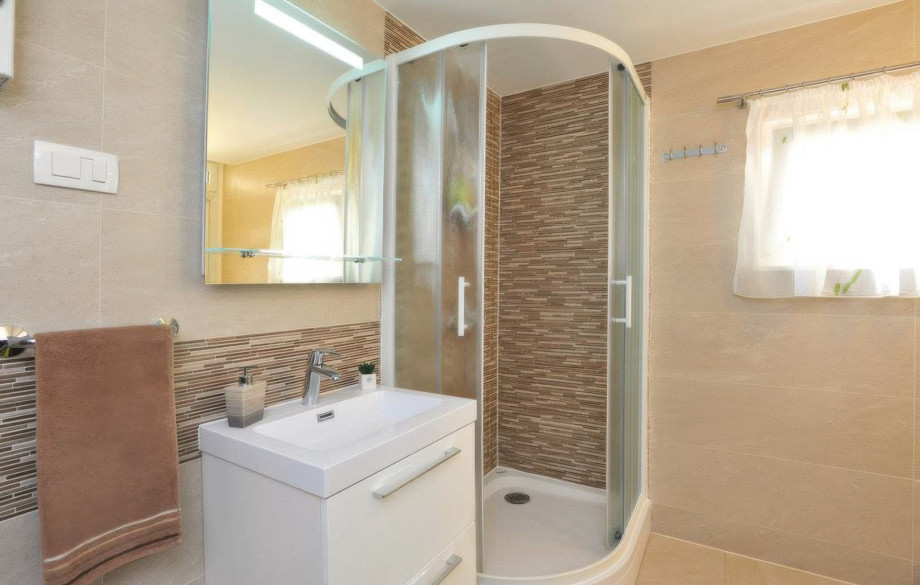 Another bathroom features stylish tiling and a curved glass shower cabin, along with a contemporary vanity unit.